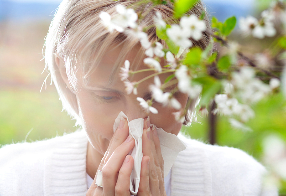 Frau putzt sich mit Taschentuch die Nase und ist auf dem Weg zur Blutspende trotz Allergie