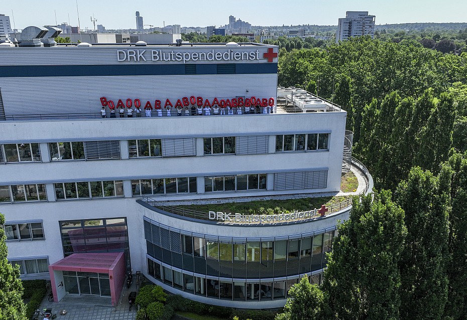 Gebäude des DRK-Blutspendedienst Baden-Württemberg - Hessen in Frankfurt, Mitarbeitende stehen auf dem Dach und halten rote Luftballons in die Luft