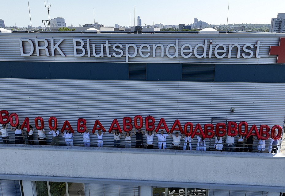 Gebäude des DRK-Blutspendedienst Baden-Württemberg - Hessen in Frankfurt, Mitarbeitende stehen auf dem Dach und halten rote Luftballons in die Luft