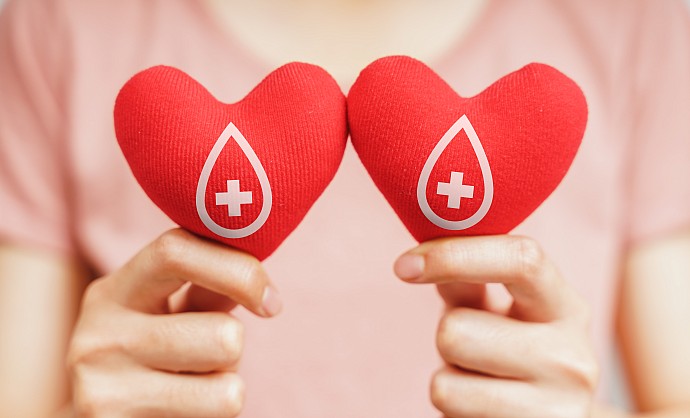 Frauenhände halten zwei rote Herzen mit Blutspende-Symbol