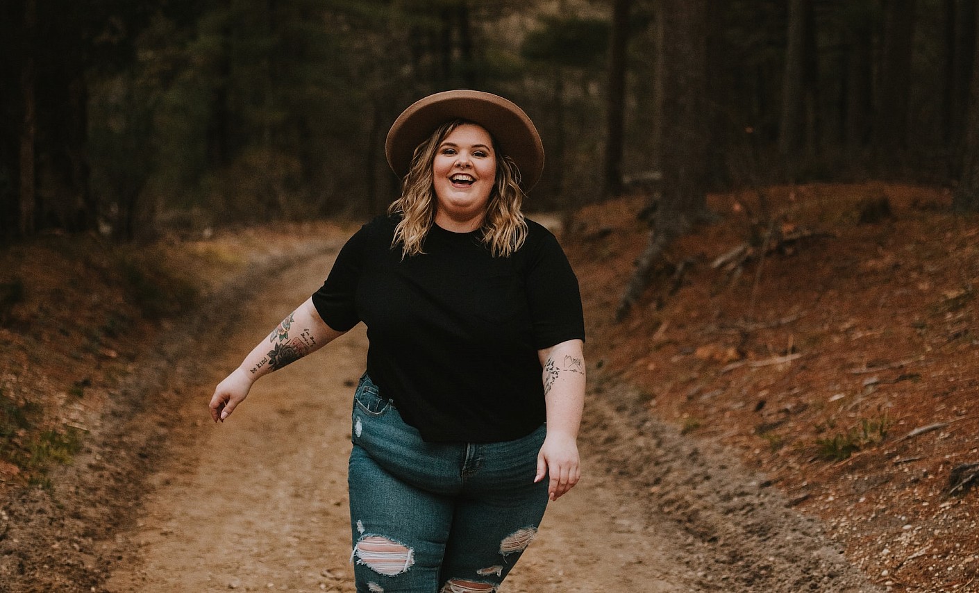 Junge dicke Frau läuft lachend und barfuß über einen Waldweg