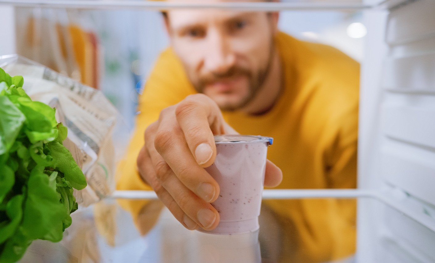 Mann nimmt Joghurt aus Kühlschrank 