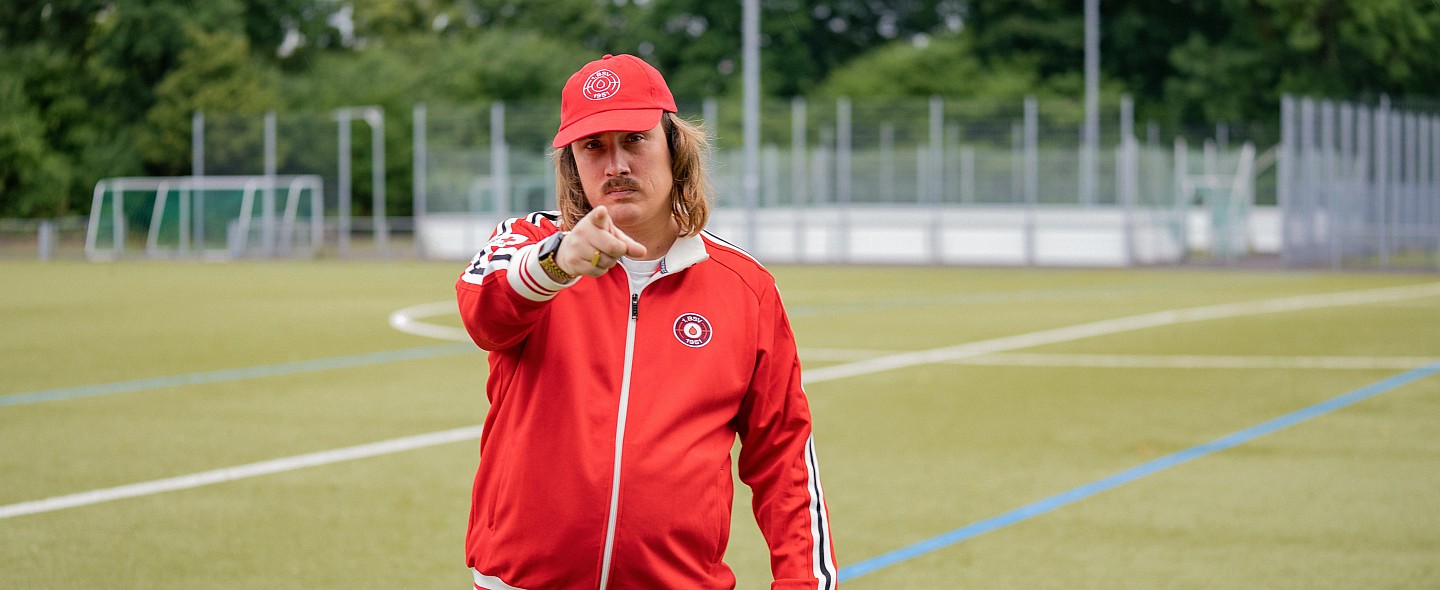 Coach Rob in rotem Trainingsanzug zeigt auf dich