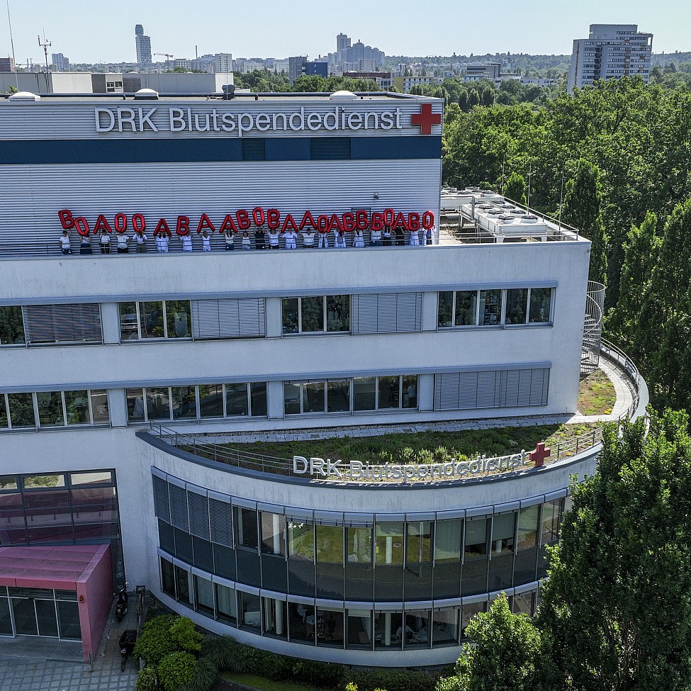 Gebäude des DRK-Blutspendedienst Baden-Württemberg - Hessen in Frankfurt, Mitarbeitende stehen auf dem Dach und halten rote Luftballons in die Luft