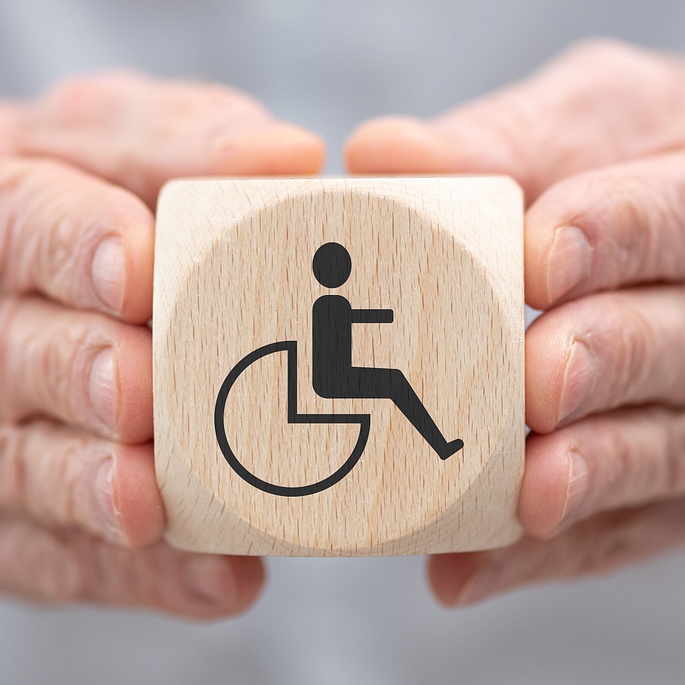 hände-halten-holzwürfel-würfel-symbol-behinderung-rollstuhl